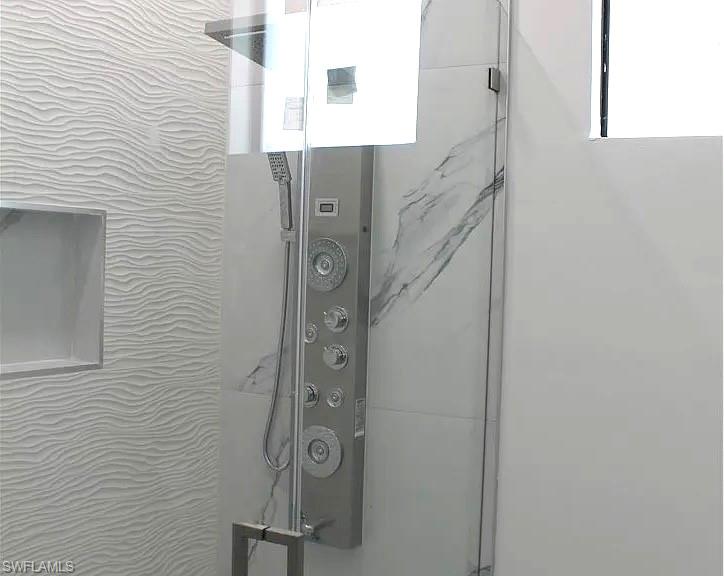 Contemporary shower enclosure featuring a multi-function shower panel with integrated handheld sprayer, clear glass door, and polished chrome hardware