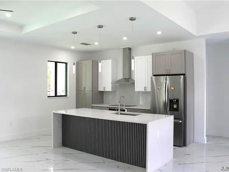 Modern kitchen featuring a waterfall island with slatted detailing, recessed and pendant lighting, stainless steel appliances, and two-tone cabinetry