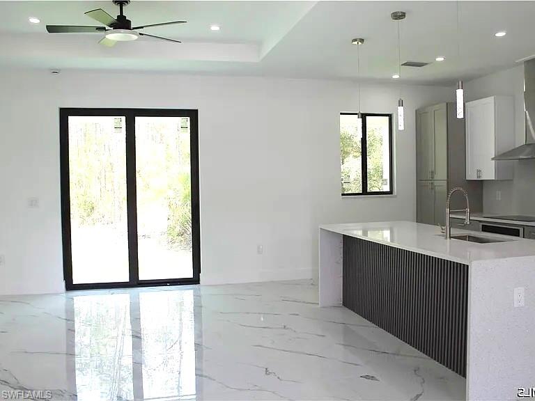 Spacious open concept interior featuring large format marble-look tile flooring, a modern kitchen island with textured paneling and white countertop, recessed lighting, and a ceiling fan