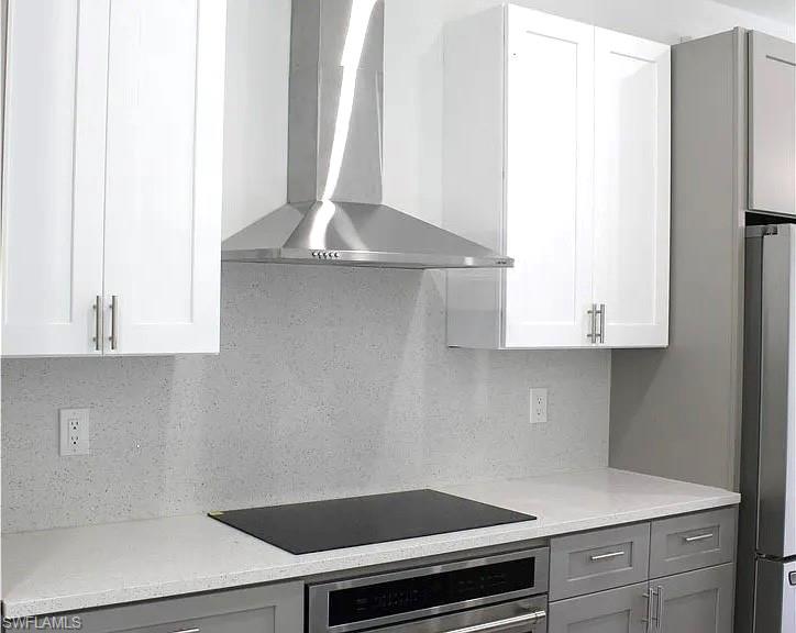 Modern kitchen featuring white upper cabinetry, gray lower cabinetry, and a stainless steel range hood