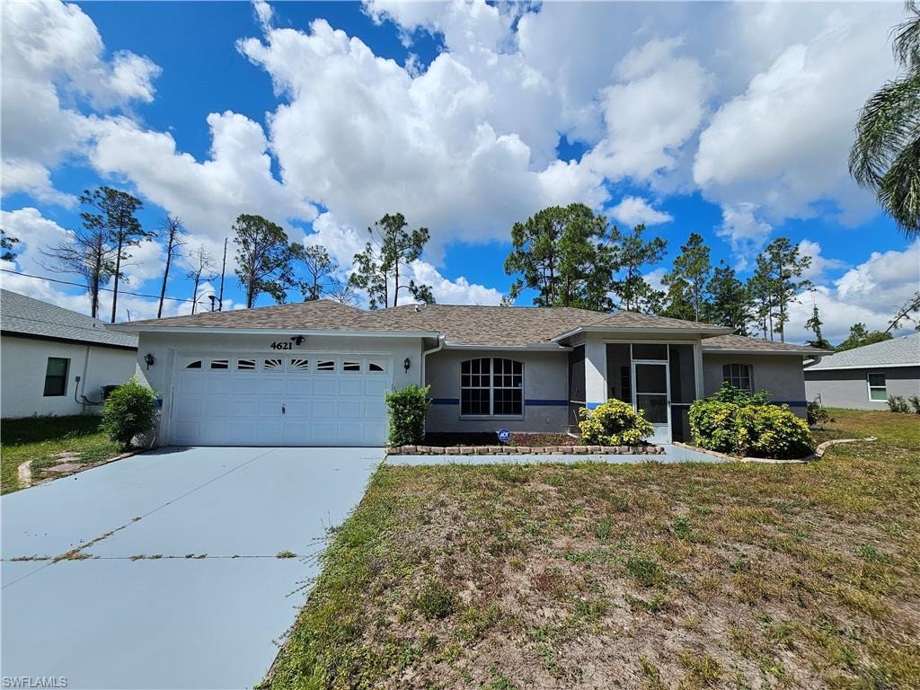 Single-story residence featuring an attached two-car garage, painted driveway, screened front entry, arched window, and mature landscaping