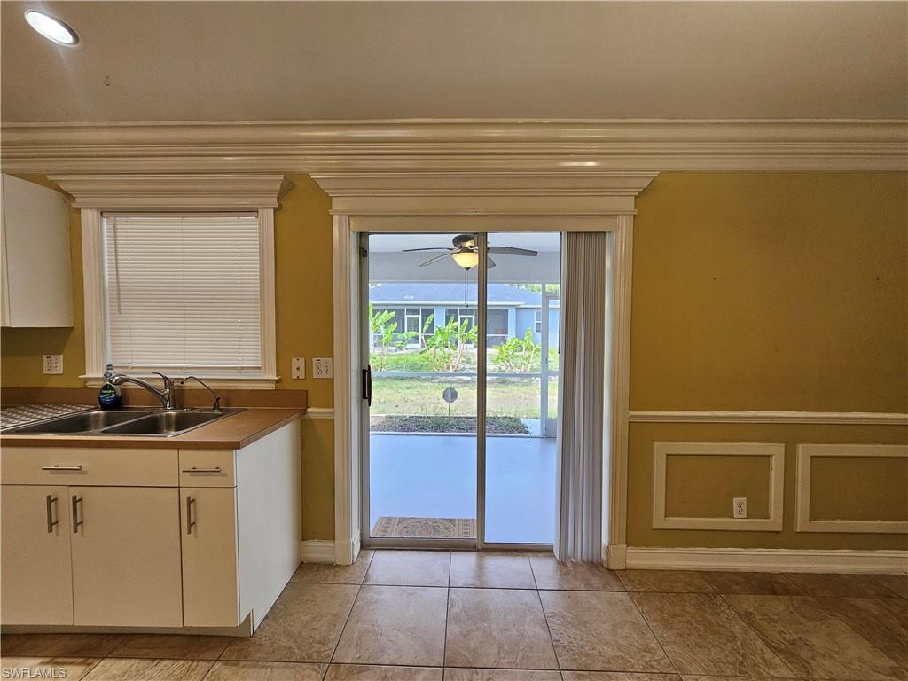 Sliding glass doors opening to a screened patio, featuring an adjacent kitchen area with white cabinetry, a double basin sink, and wood-finish countertops