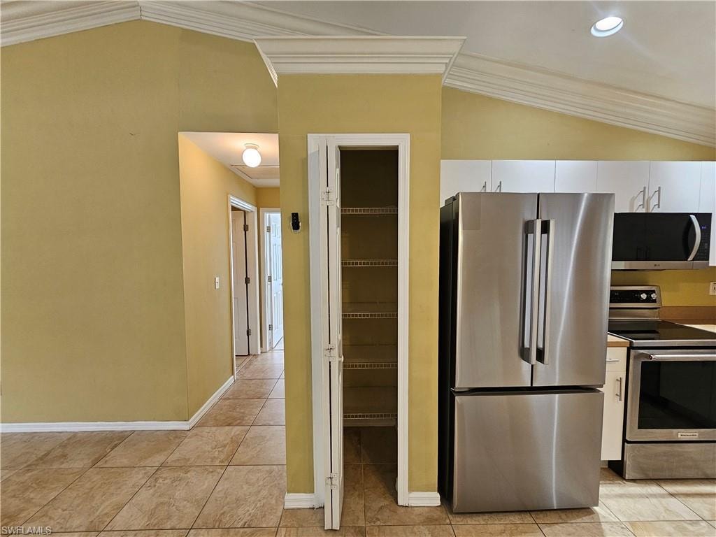 Kitchen area featuring vaulted ceilings with crown molding, stainless steel appliances, white cabinetry, and tile flooring