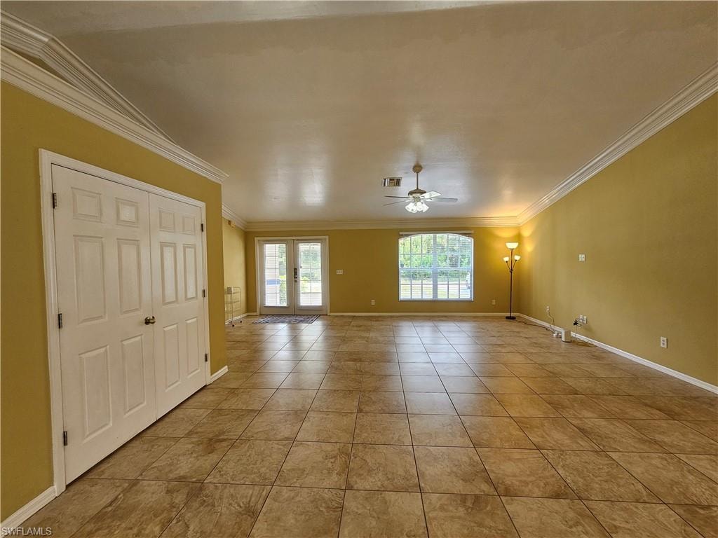 Spacious interior room featuring large format tile flooring, crown molding, double French doors, a ceiling fan with light fixture, and a large arched window