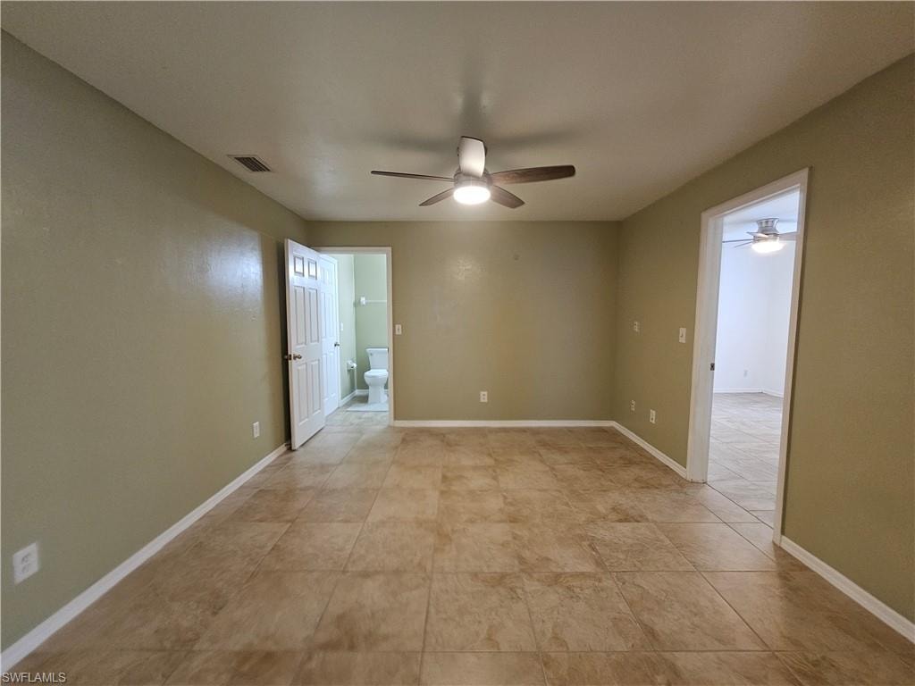 Spacious interior room featuring neutral wall paint, tile flooring, and a ceiling fan
