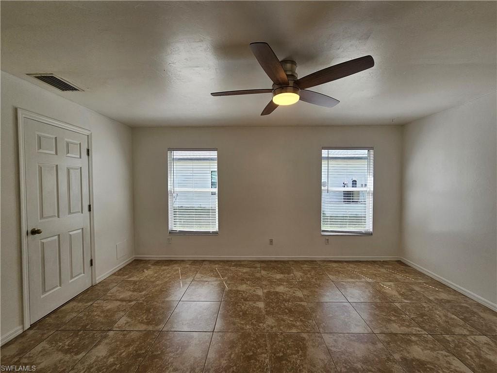 Spacious room featuring tile flooring, two windows with blinds, a ceiling fan with integrated lighting, and a paneled door