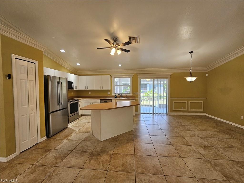 Open-concept living area featuring a kitchen island, stainless steel appliances, tile flooring, crown molding, and sliding glass doors