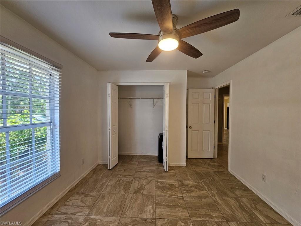 Spacious room featuring large window with blinds, wood-finish ceiling fan with integrated lighting, tiled flooring, and bifold closet doors