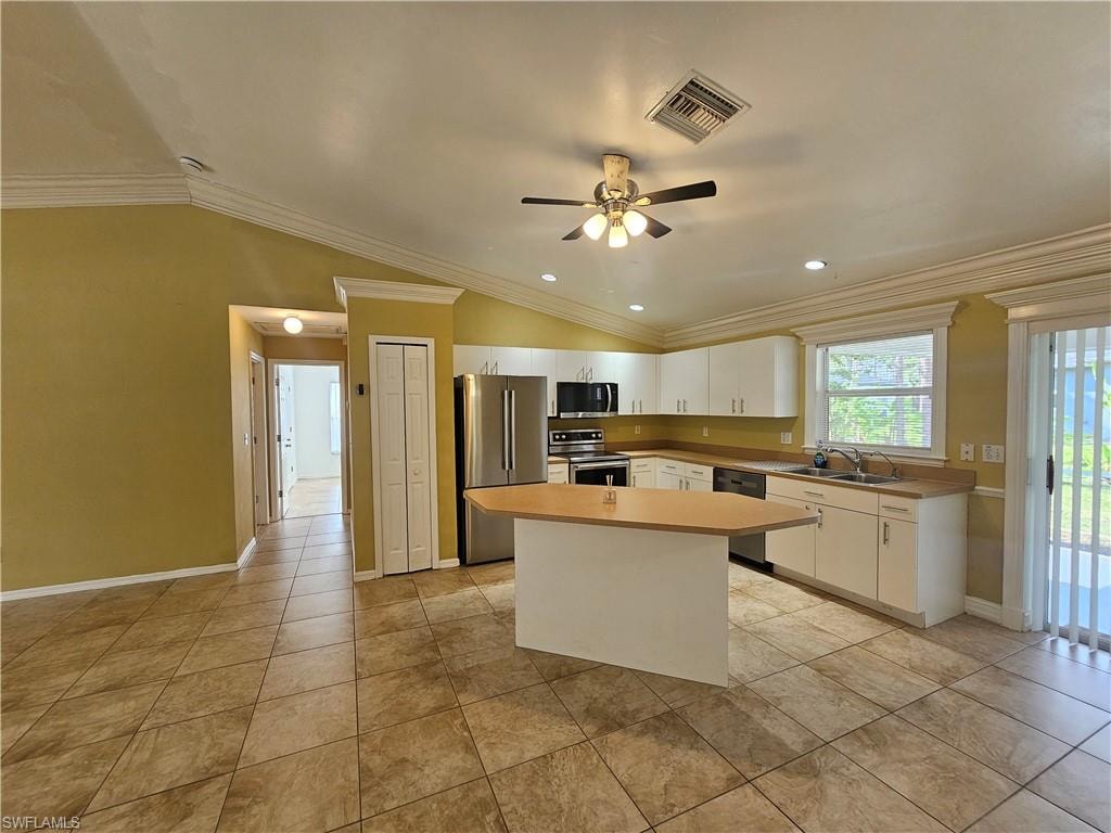 Open-concept kitchen featuring an island with breakfast bar, stainless steel appliances, white cabinetry, and a double basin sink