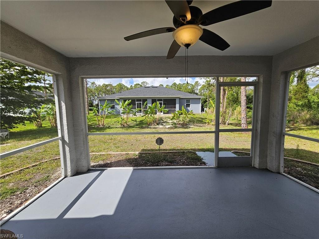 Screened patio featuring a ceiling fan with integrated lighting, a concrete floor, and an expansive exterior lawn area