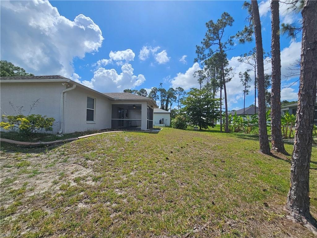 Expansive rear lawn featuring a screened patio, mature trees, and a stucco exterior