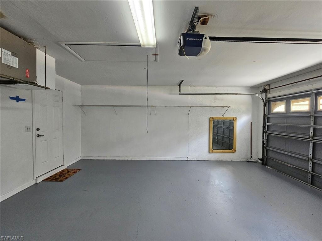 Spacious garage featuring a painted concrete floor, fluorescent ceiling lighting, an automatic garage door opener, and integrated wall shelving