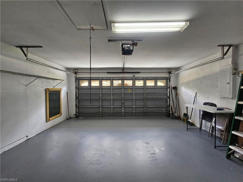 Spacious garage featuring a durable concrete floor, an overhead door with transom-style windows, and a built-in access panel