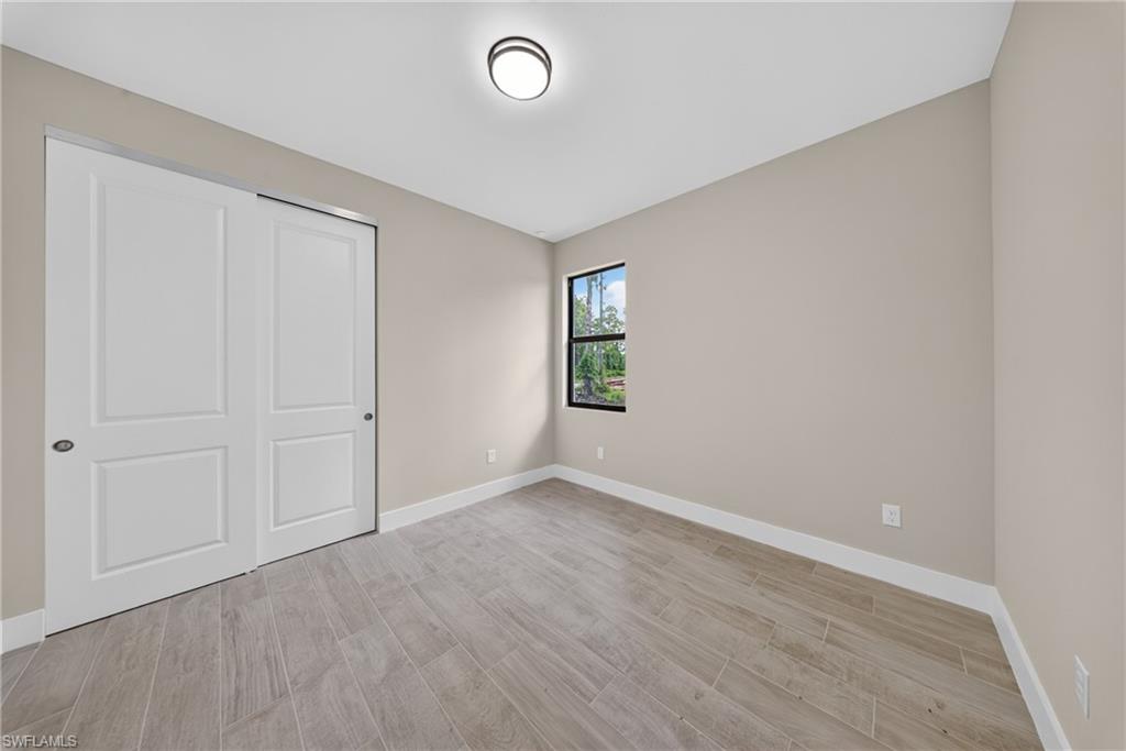 Bedroom featuring light neutral wall paint, wood-look tile flooring, a window with black trim, a flush-mount ceiling light, and white bi-fold closet doors