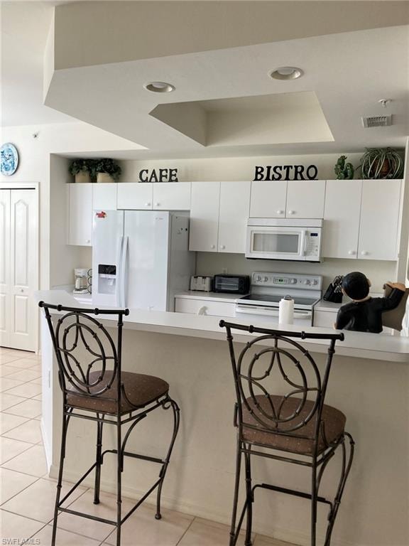 Kitchen with white appliances, a tray ceiling, light tile patterned floors, a breakfast bar area, and white cabinets