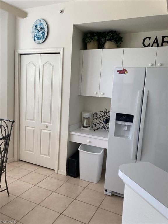 Kitchen featuring white fridge with ice dispenser, light countertops, white cabinetry, and light tile patterned flooring