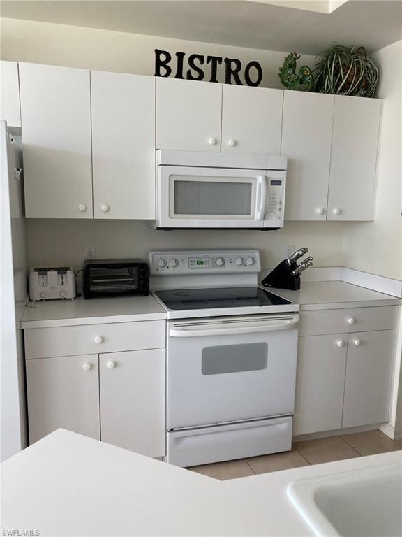 Kitchen featuring white appliances, white cabinets, light countertops, and light tile patterned floors