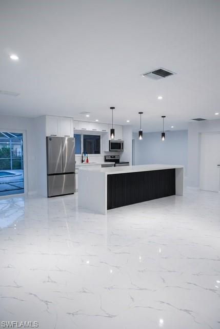 Open-concept kitchen featuring a waterfall island with a black slatted base, stainless steel appliances, white cabinetry, and white marble-look tile flooring