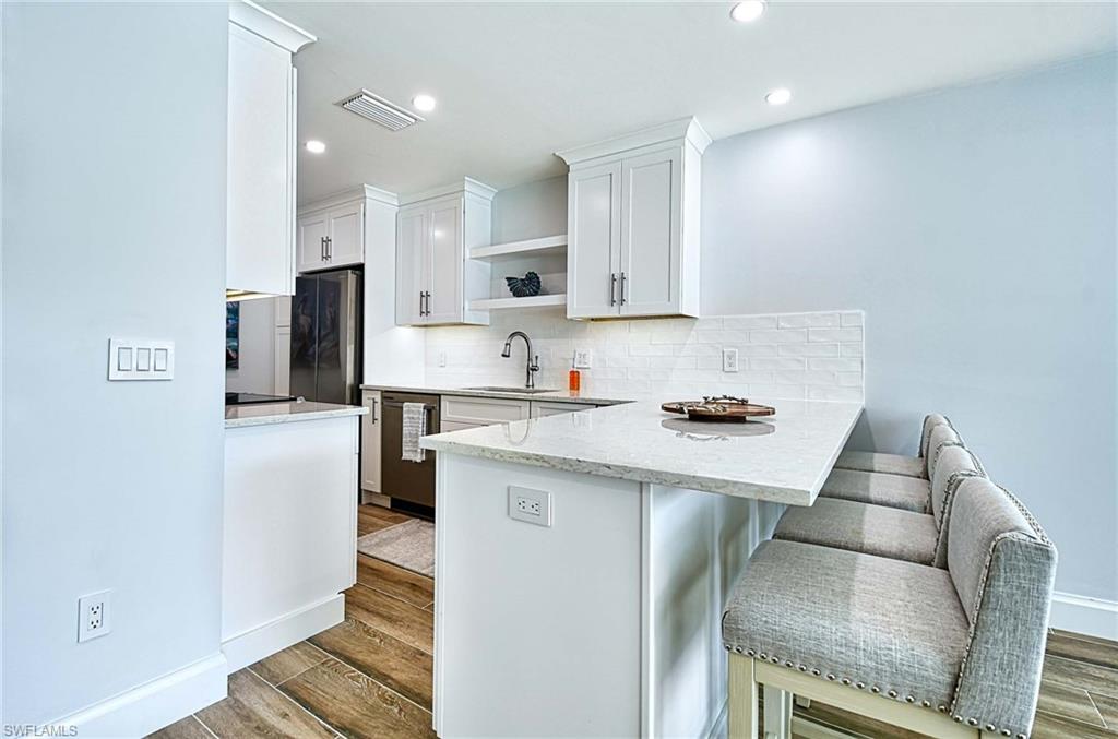 Kitchen featuring white cabinetry, kitchen peninsula, hardwood / wood-style floors, backsplash, and sink