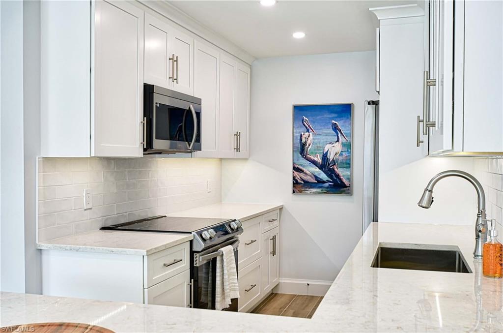 Kitchen featuring electric stove, light wood-type flooring, backsplash, sink, and white cabinets