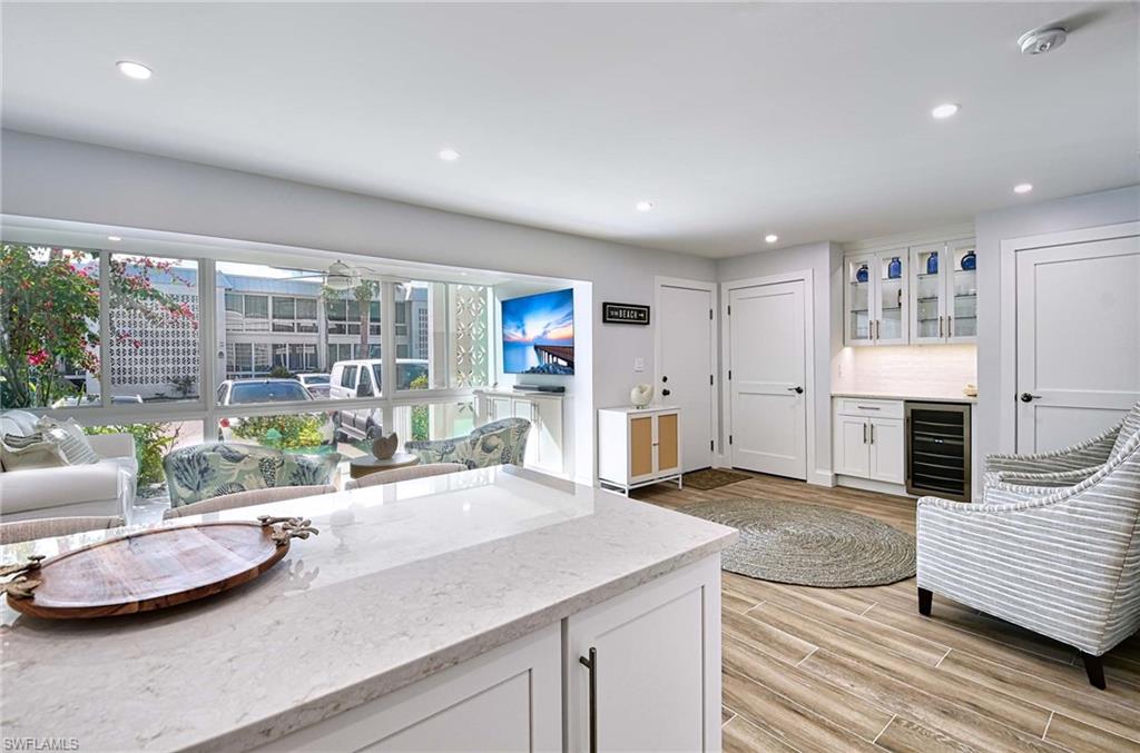 Kitchen featuring light hardwood / wood-style floors, beverage cooler, tasteful backsplash, light stone countertops, and white cabinets