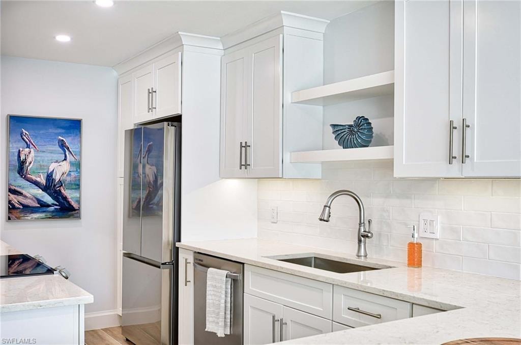 Kitchen featuring white cabinetry, light wood-type flooring, stainless steel appliances, light stone counters, and tasteful backsplash