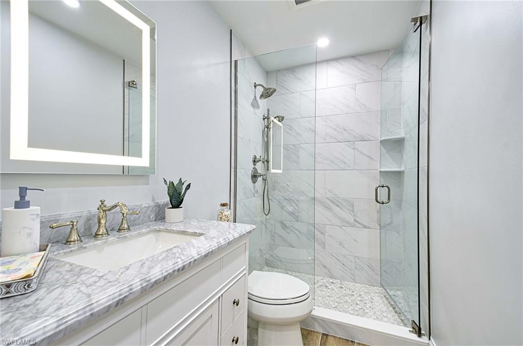 Bathroom with a shower with shower door, toilet, and large vanity
