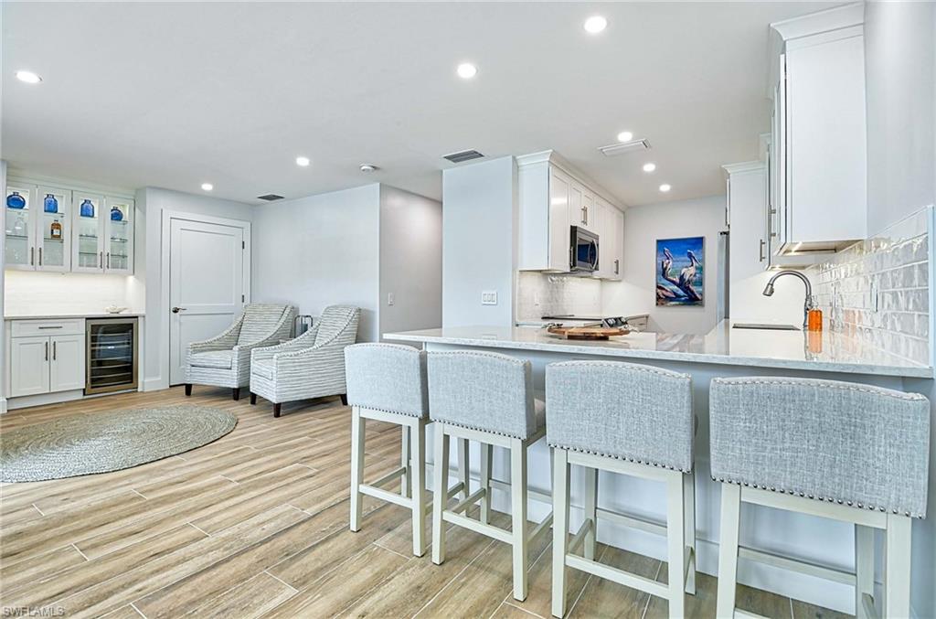 Kitchen with beverage cooler, backsplash, a kitchen bar, white cabinetry, and sink