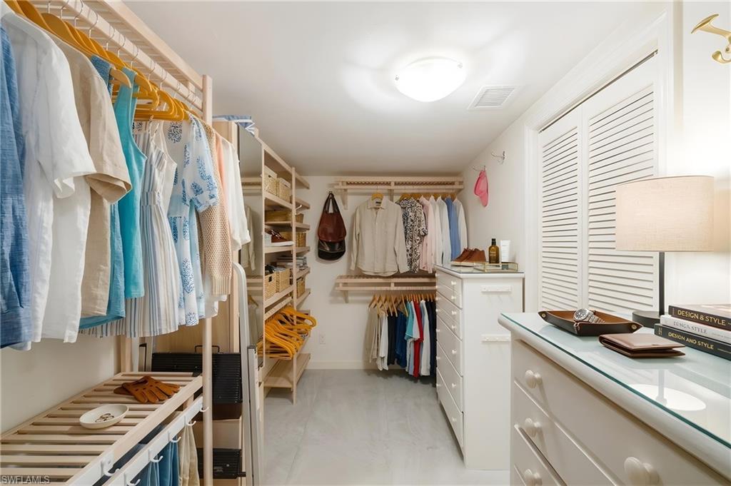Spacious walk-in closet featuring extensive built-in shelving, multiple hanging rods, a central dresser, and louvered bifold doors