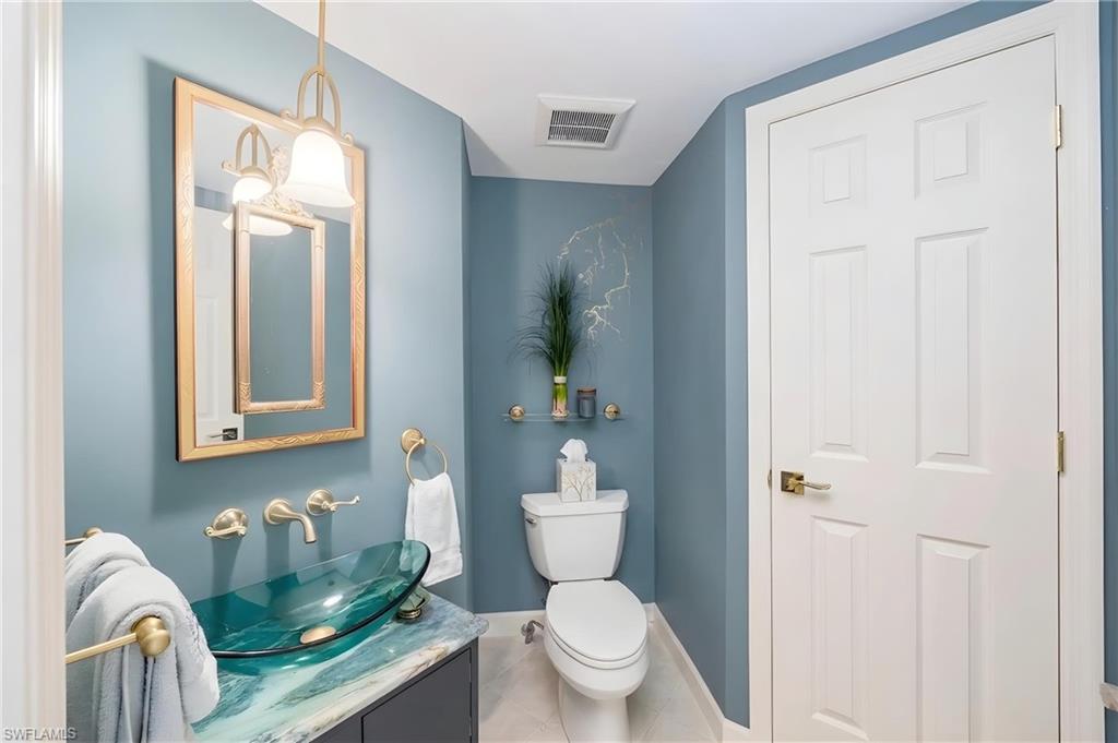 Powder room featuring a vessel sink with a glass basin, wall-mounted faucet, framed mirror, and a built-in toilet