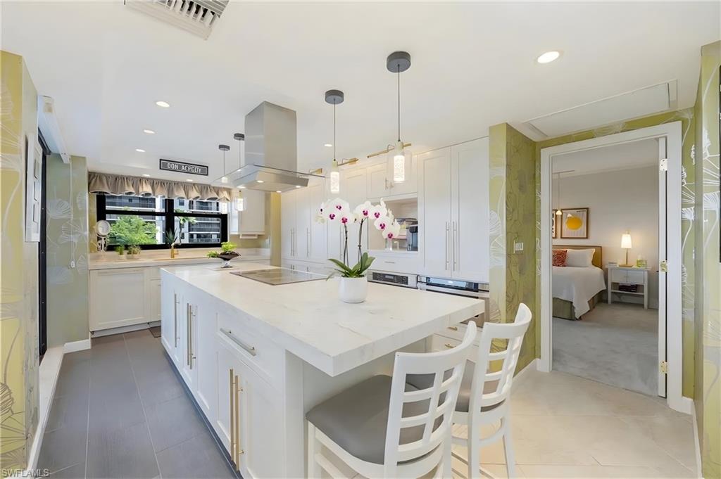 Contemporary kitchen featuring a large center island with integrated cooktop, white cabinetry, and stainless steel appliances