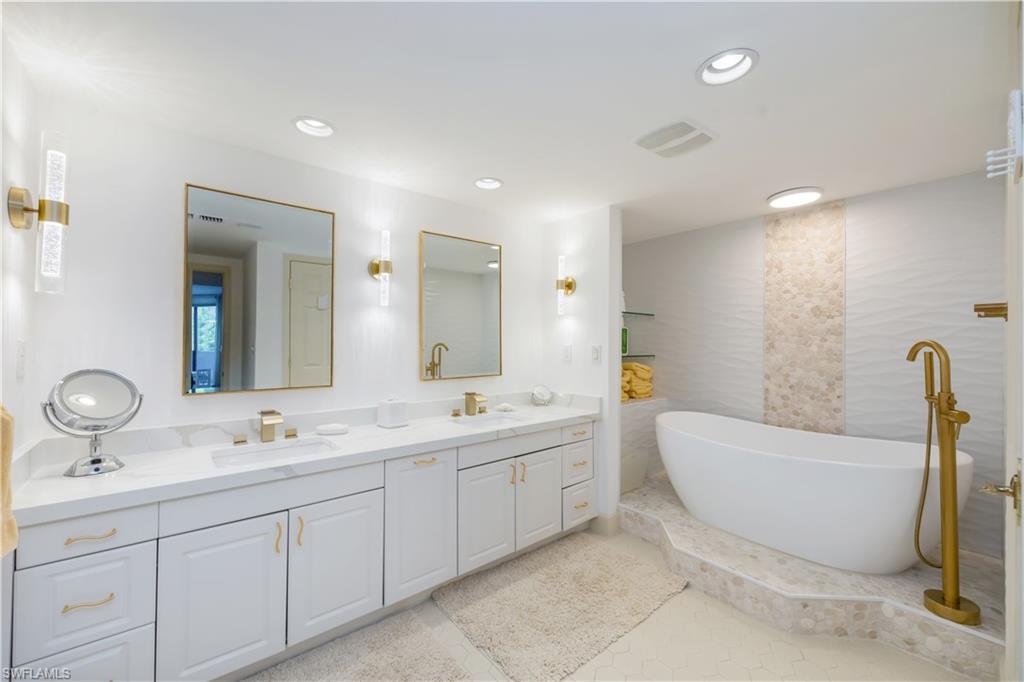 Bathroom featuring a freestanding soaking tub with a floor-mounted faucet, a double vanity with undermount sinks, stone countertops, and gold-finish fixtures