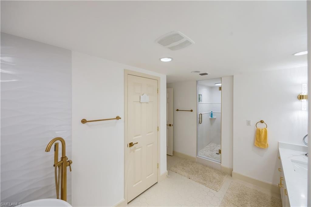 Modern bathroom featuring a freestanding tub with a gold-finish floor-mounted faucet, a clear glass enclosed shower, and a vanity with a white countertop