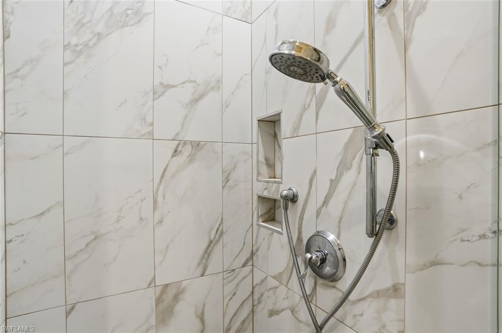Shower enclosure featuring large format white tiled walls with grey veining, a chrome shower head with a flexible hose, and two recessed wall niches