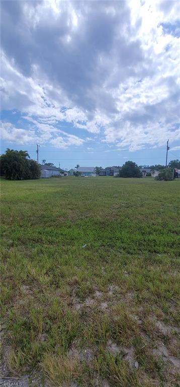 Expansive cleared lot featuring natural grass ground cover and distant residential structures