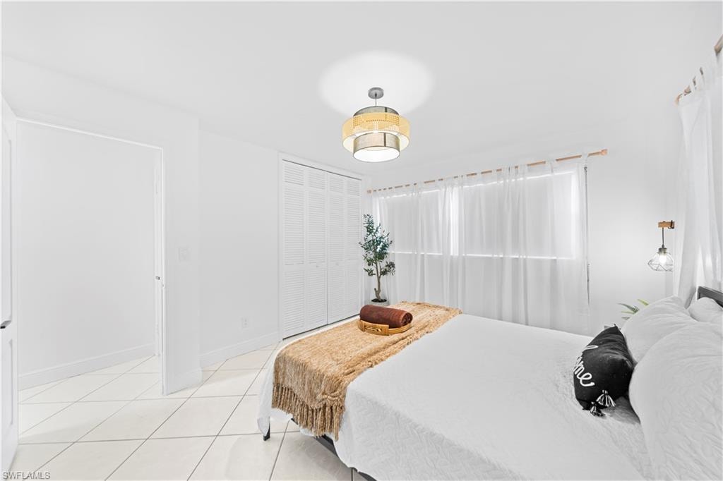 White tile flooring with geometric grout lines, a window featuring sheer white drapery, louvered bi-fold closet doors, a decorative ceiling fixture, and a wall-mounted lighting fixture