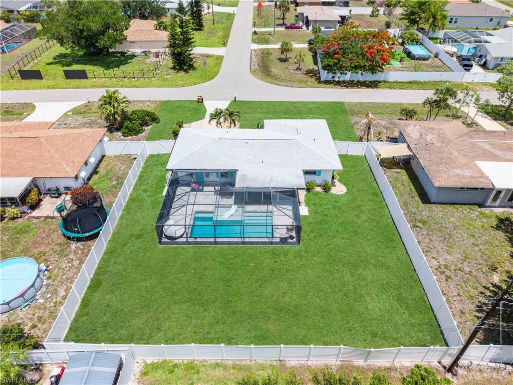 Single-story residence featuring a screened-in swimming pool, manicured lawn, and white privacy fencing