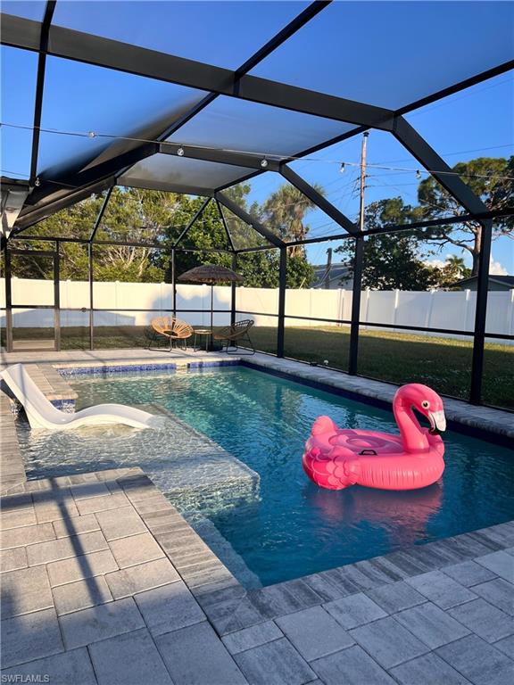 Screened-in pool area featuring a blue-tiled swimming pool with integrated steps and sun shelf, paver decking, and a white privacy fence