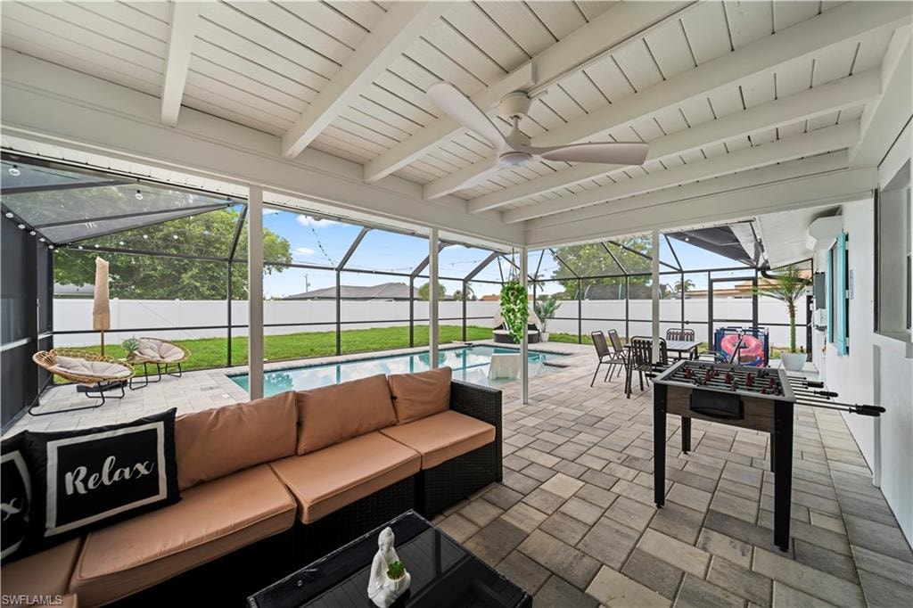 Screened patio featuring a paved floor, exposed beam ceiling with a ceiling fan, and string lighting