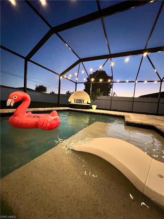 Screened pool enclosure featuring a pool with a built-in water feature and string lights