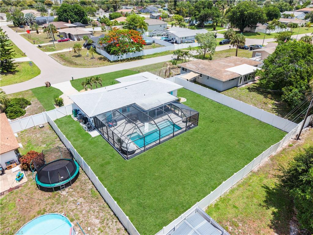Fenced property featuring a screened-in pool, expansive manicured lawn, and a light-colored roof