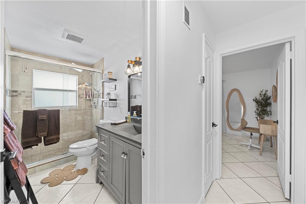 Bathroom featuring a glass-enclosed shower with tile surround, a single vanity with gray cabinetry and integrated sink, and tile flooring
