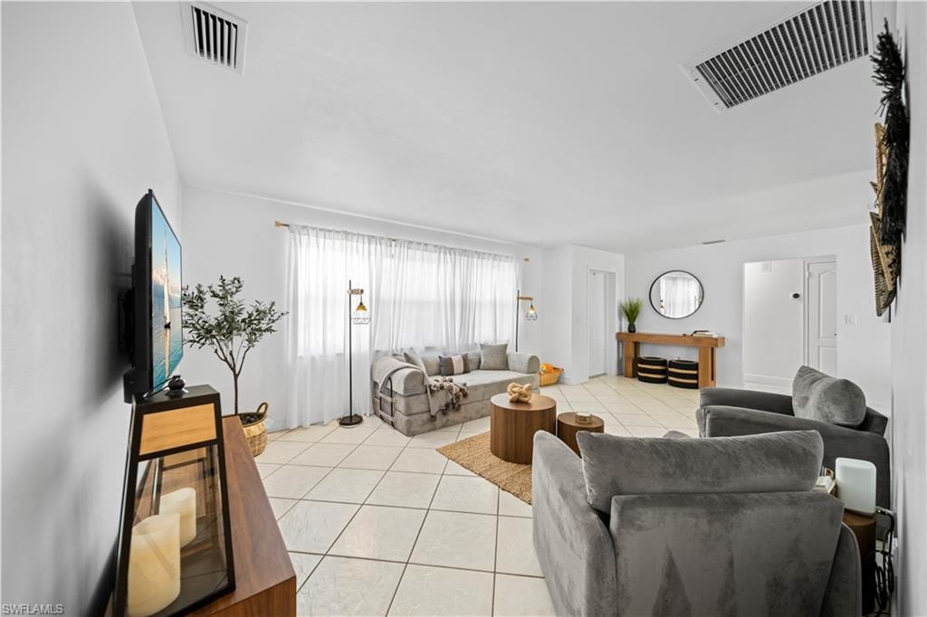 Spacious living area featuring light-colored tile flooring, white walls, and a large window with sheer white coverings