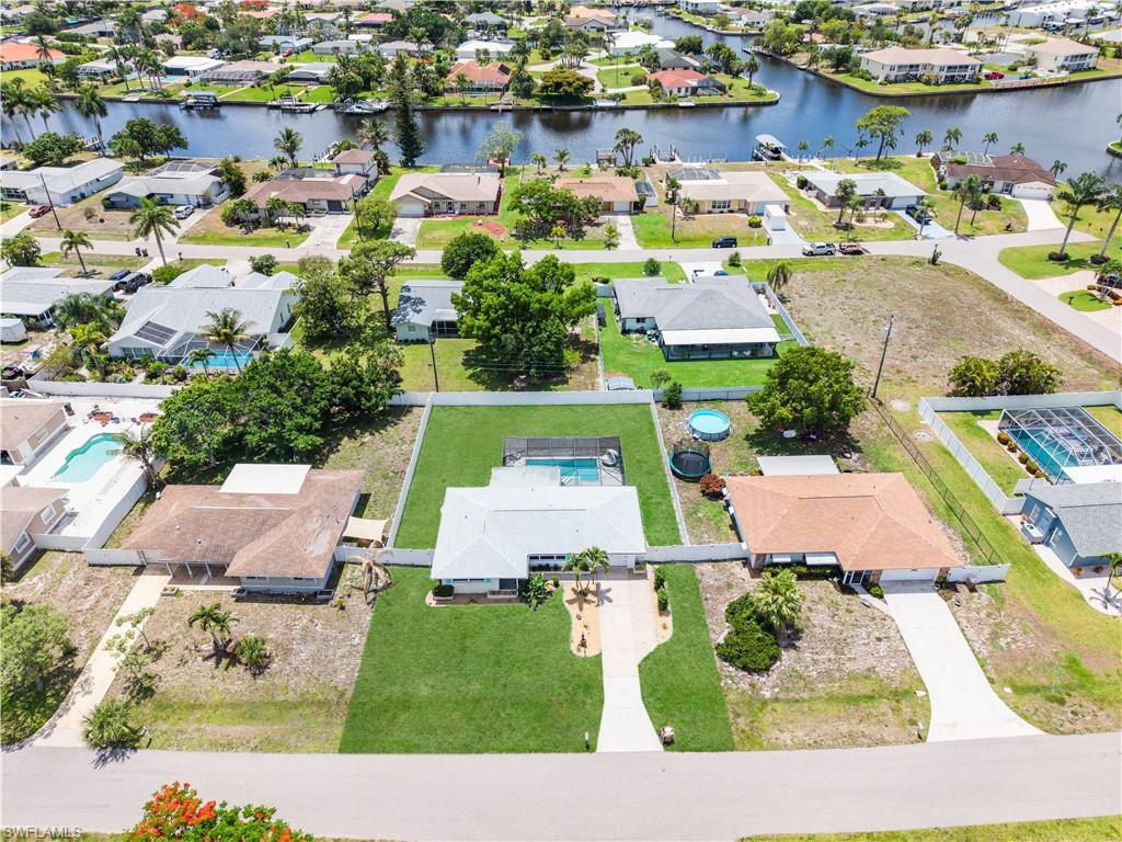 Aerial perspective showcasing a residential lot with a paved driveway, front lawn, and mature palm trees