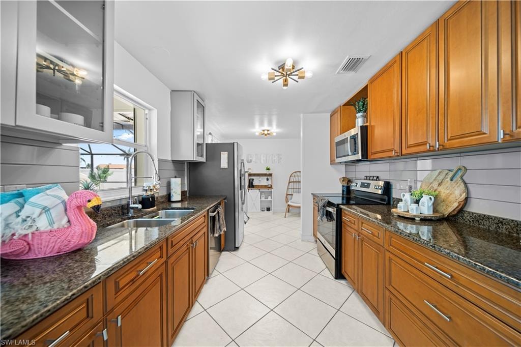 Galley kitchen featuring wood cabinetry, dark stone countertops, and stainless steel appliances