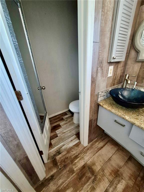 Bathroom featuring wood-finish flooring, a vanity with a granite-look countertop, a blue vessel sink, and a wall-mounted medicine cabinet
