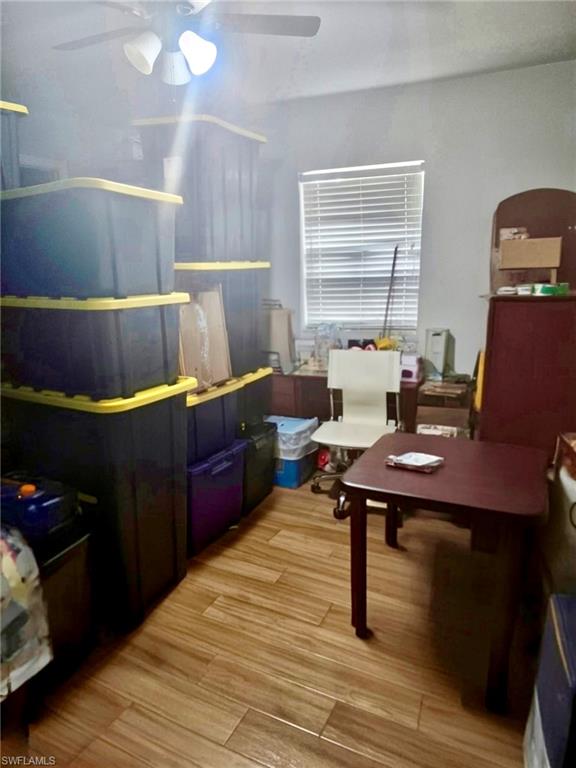 Interior room featuring wood-finish flooring, a single window with horizontal blinds, and a ceiling fan with integrated lighting