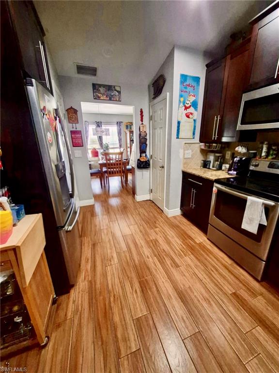 Kitchen featuring wood-finish flooring, dark wood cabinetry, stainless steel appliances, and granite countertops