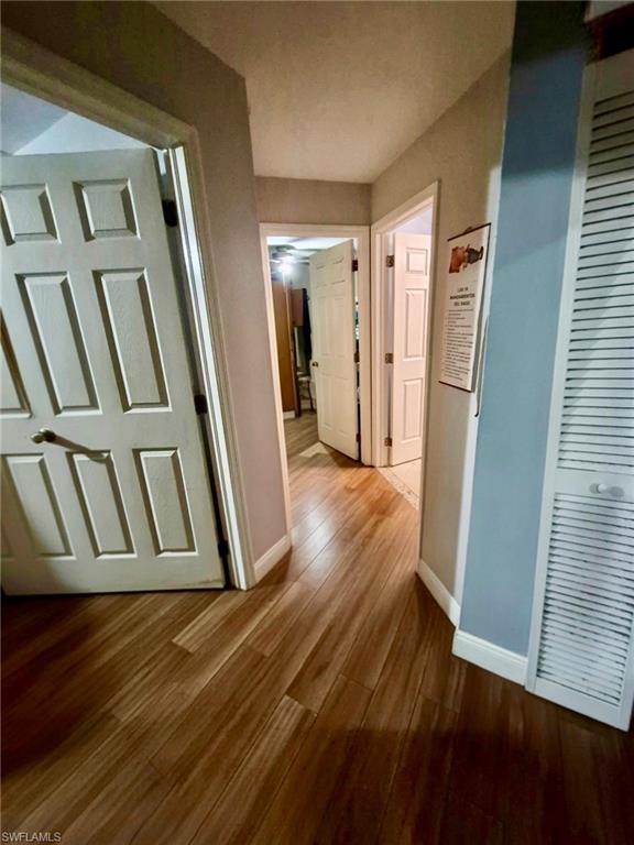 Wood-finish flooring throughout a hallway with multiple paneled doors and louvered closet doors