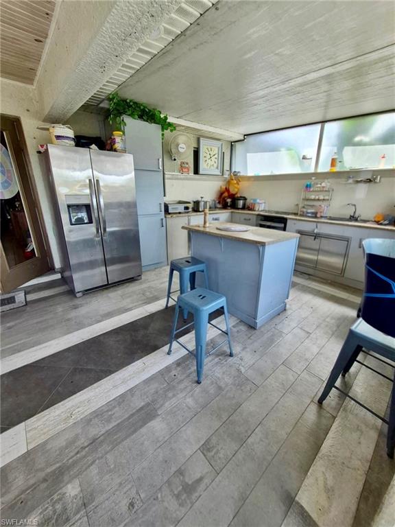 Kitchen featuring wood-finish flooring with a contrasting central inlay, a freestanding island with a wood-finish countertop, stainless steel refrigerator, and a continuous band of upper windows